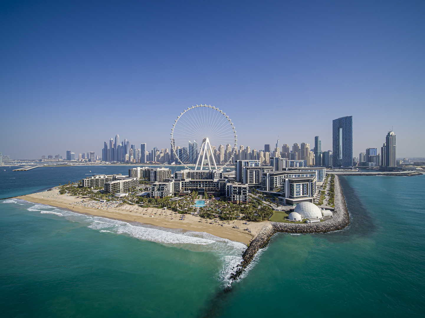 Aerial view of Bluewaters Island featuring Banyan Tree Dubai with Ain Dubai Ferris wheel at the center, surrounded by turquoise waters and the iconic Dubai Marina skyline in the background.